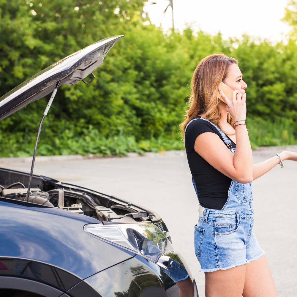 young woman and broken car calling for help on cell phone